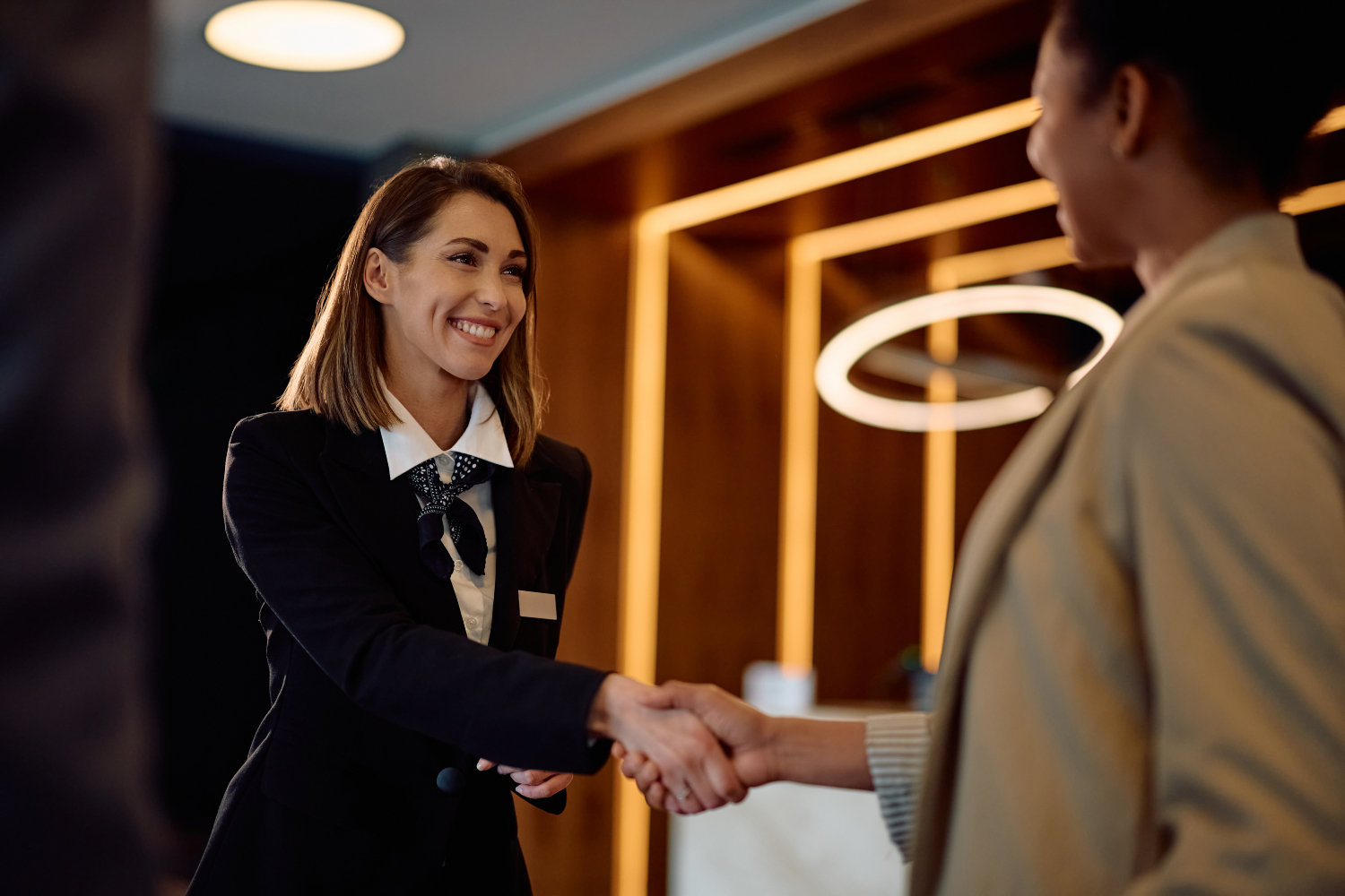 Happy hotel manager greeting African American female guest in a hallway.