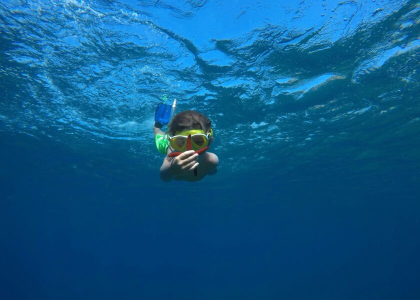 Child snorkelling in clear turquoise water holding a starfish at Koh Tao Thailand
